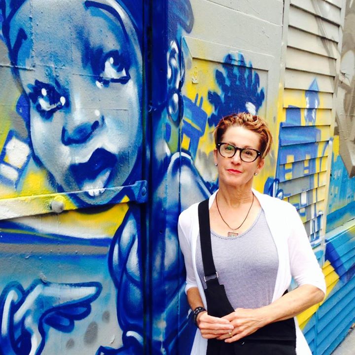 Author Lee Kvern leans against a mural on the side of a building.
